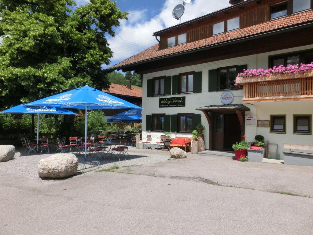 阿尔高内的伊门施塔特Goldiger Hirsch的一个带蓝伞和椅子的庭院和一座建筑