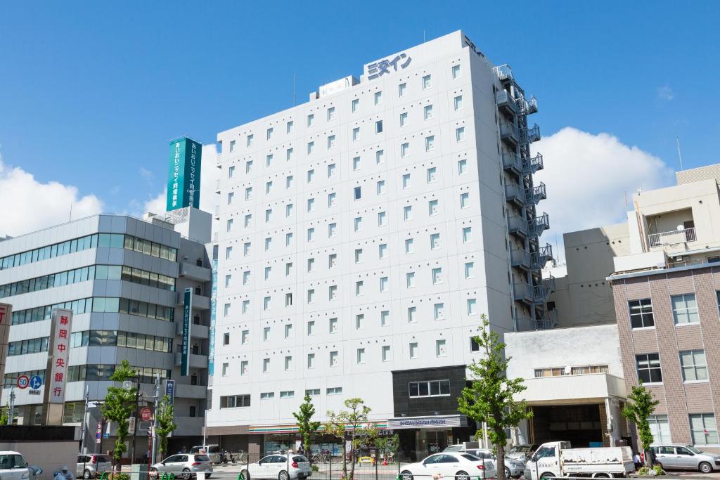 静冈静冈北口桑科酒店的一座白色的建筑,前面有汽车停放