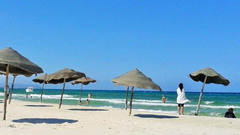 Ḩammām al Ghazzāzstudio climatise pour vacance的站在海滩上,戴着草伞的女人