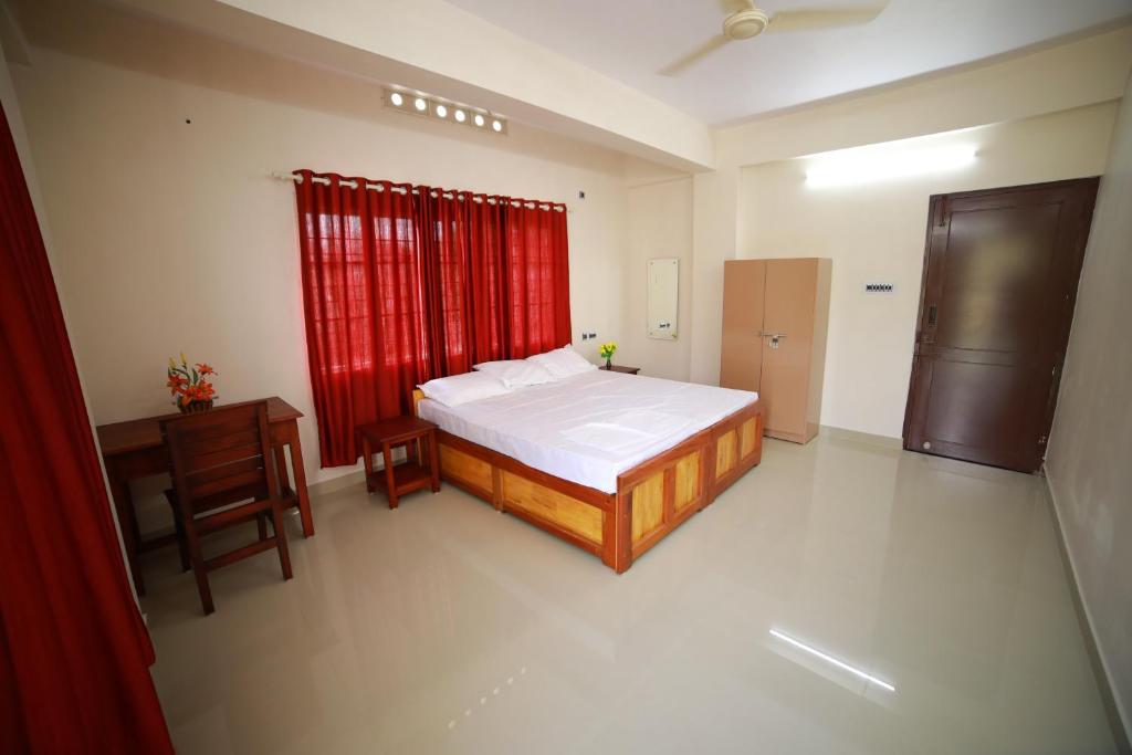 特里凡得琅Indeevaram Residency的一间卧室配有一张床、一张书桌和红色窗帘