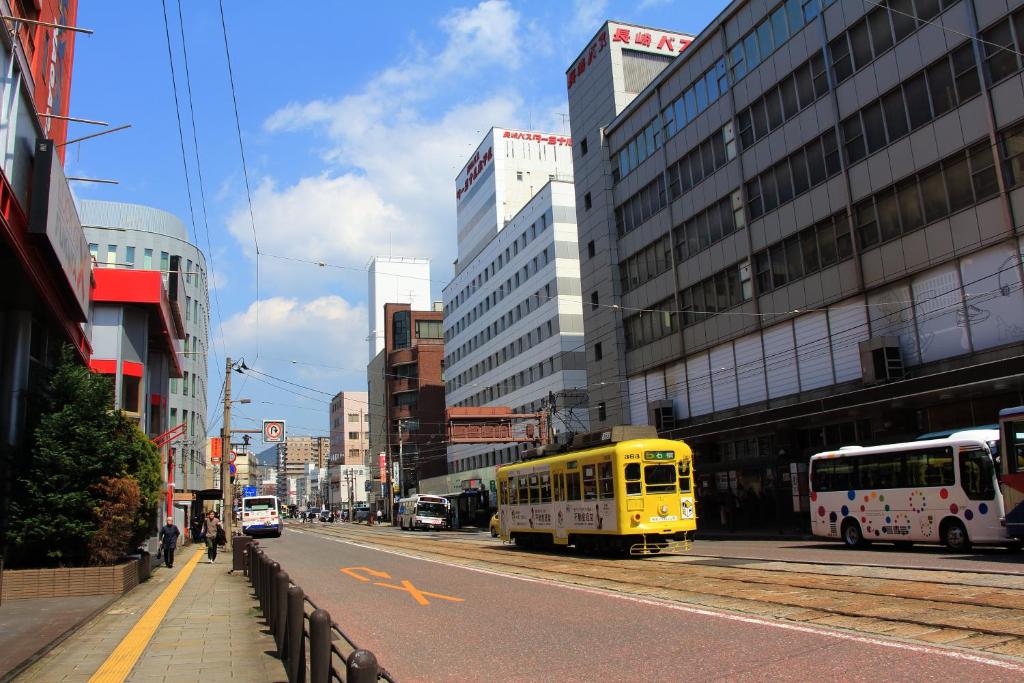 长崎Nagasaki Bus Terminal Hotel的一辆黄色的巴士驶向城市街道,街道上有许多建筑
