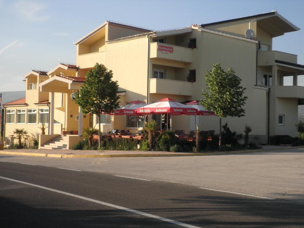 Hrvace扬科维奇汽车旅馆的街道旁的一座带桌子和遮阳伞的建筑