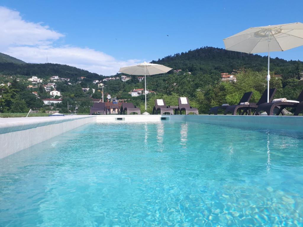 奥帕提亚Guest House Stancija Kovacici的蓝色海水游泳池和遮阳伞