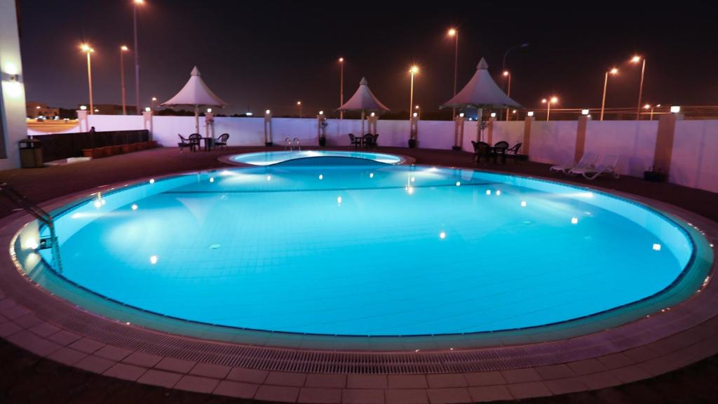 锡卜Remas Hotel Suites - Al Khoudh, Seeb, Muscat的夜间大型蓝色游泳池