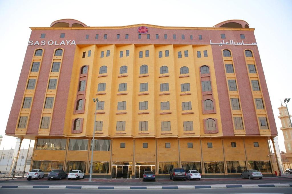阿可贺巴SAS Al Olaya Hotel Suites的一座黄色的大建筑,前面有汽车停放