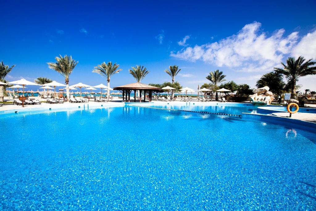 拉斯苏德尔Mousa Coast Hotel & Spa的一座种植了棕榈树和遮阳伞的大型蓝色游泳池