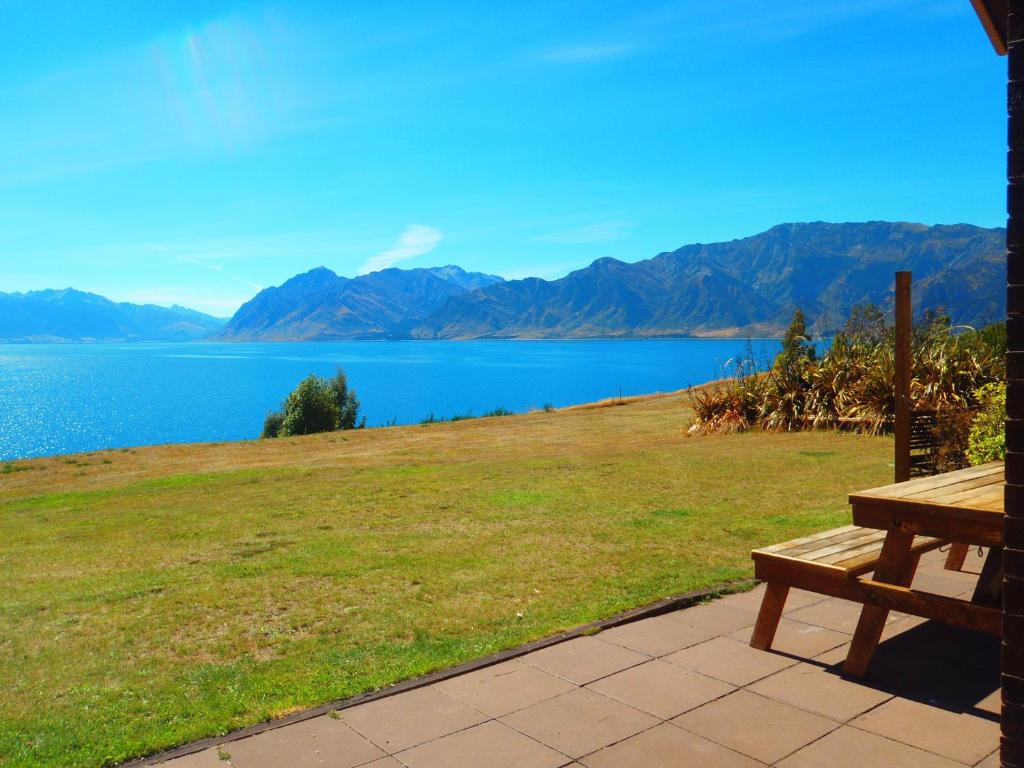 哈威亚湖Lakefront Bellevue Lake Hawea Wanaka的木凳坐在湖边田野顶部