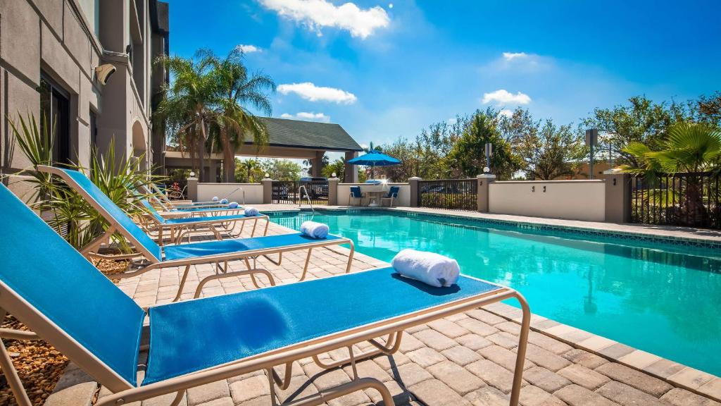 迈尔斯堡Best Western Airport Inn Fort Myers的一座带蓝色躺椅的游泳池,位于大楼旁