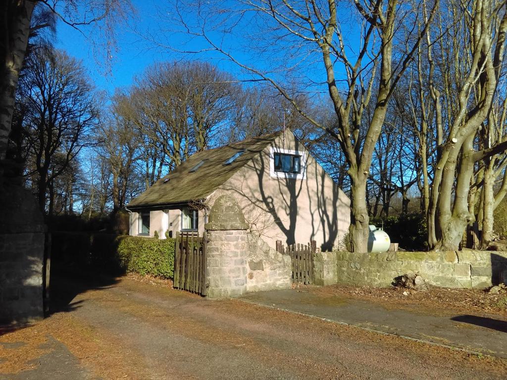 爱丁堡Lowood Cottage的一座小石头房子,设有围栏和树木