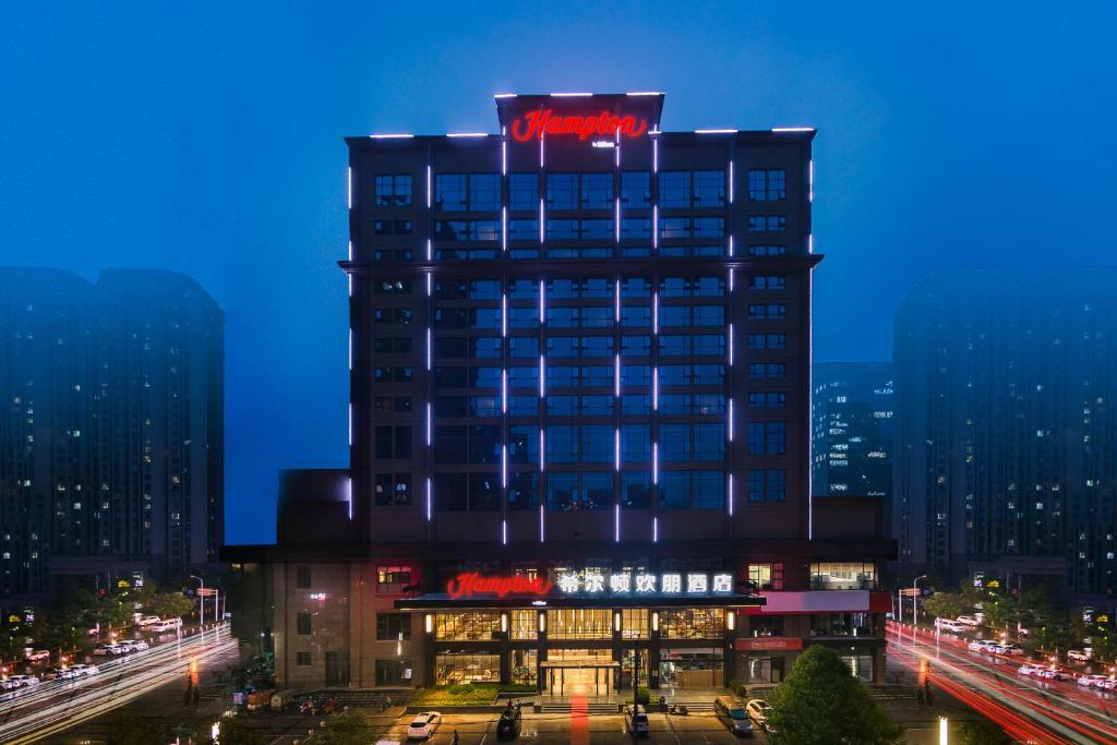 郑州郑州高新希尔顿欢朋酒店的一座高大的建筑,上面有 ⁇ 虹灯标志
