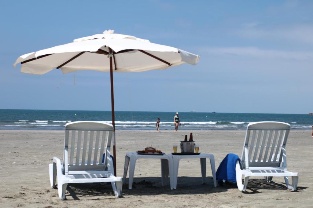巴雷克萨巴Pris Hotel的海滩上两把椅子和一张遮阳伞下的桌子