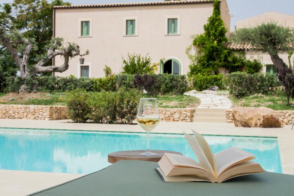 AragonaResort Fontes Episcopi的一杯葡萄酒和一本书放在游泳池畔的桌子上