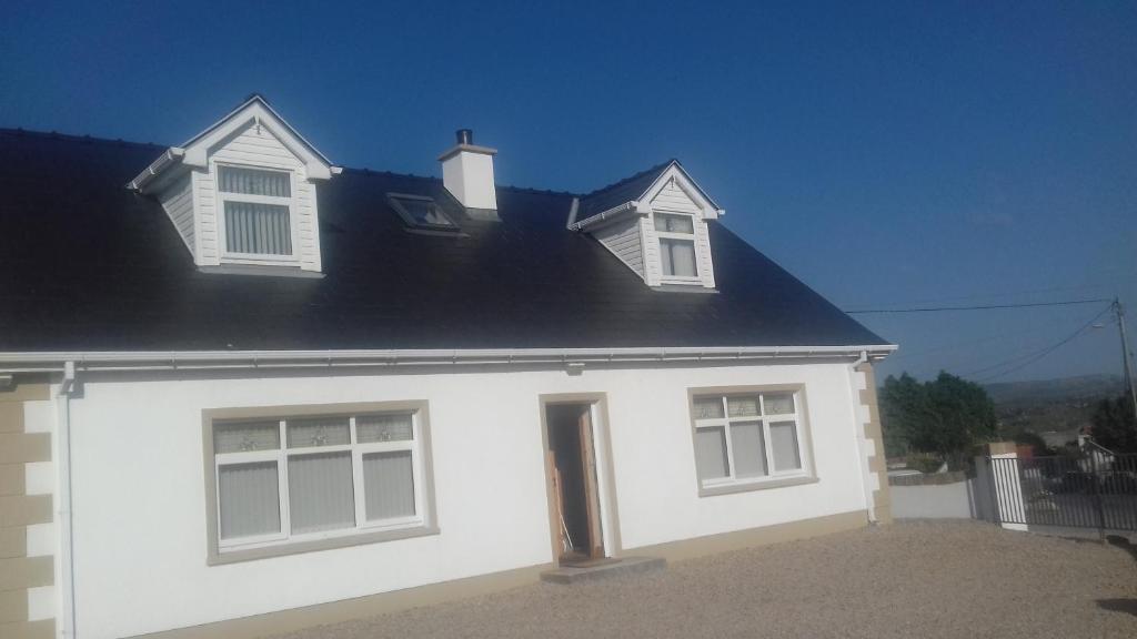 LoughanureTeach Nellie Cottage的白色的房子,设有两扇窗户和黑屋顶