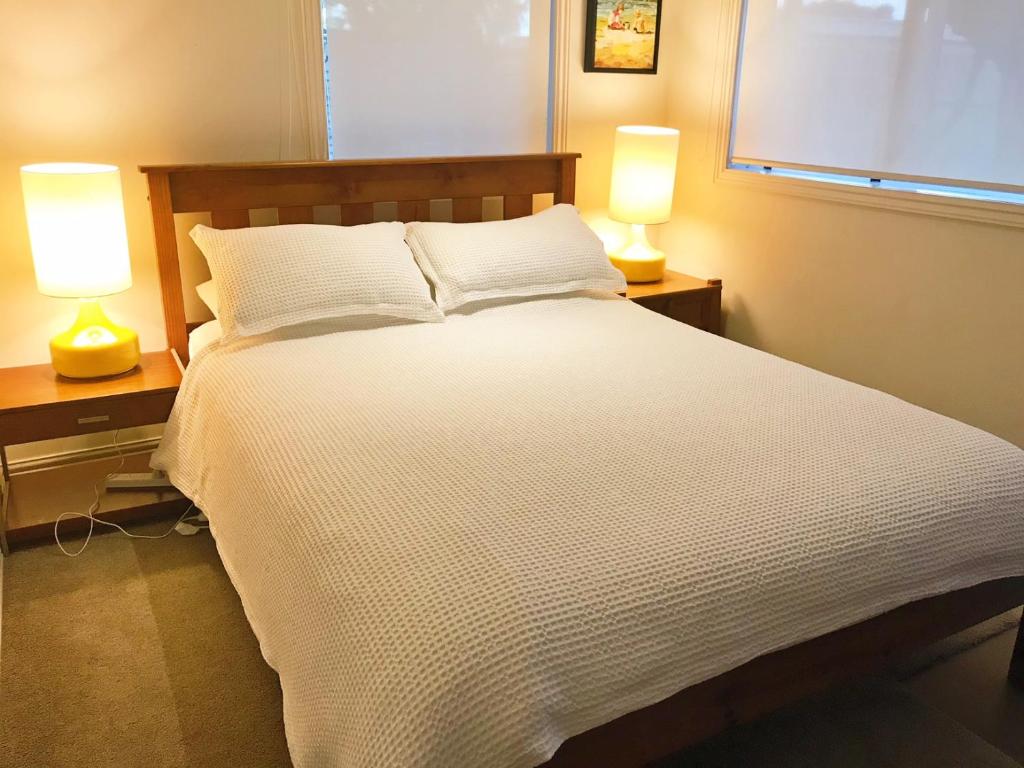 奥克兰海滩山林小屋公寓的一间卧室配有一张带两盏灯的大型白色床。