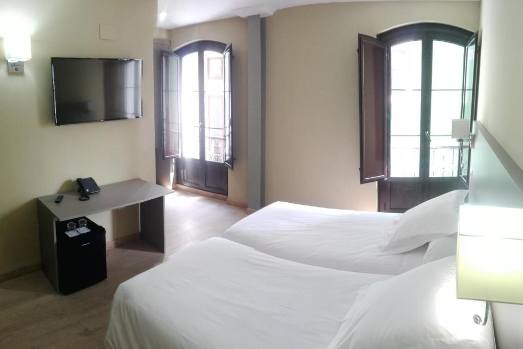 格拉多Hotel Areces的酒店客房设有两张床、一张书桌和两个窗户。