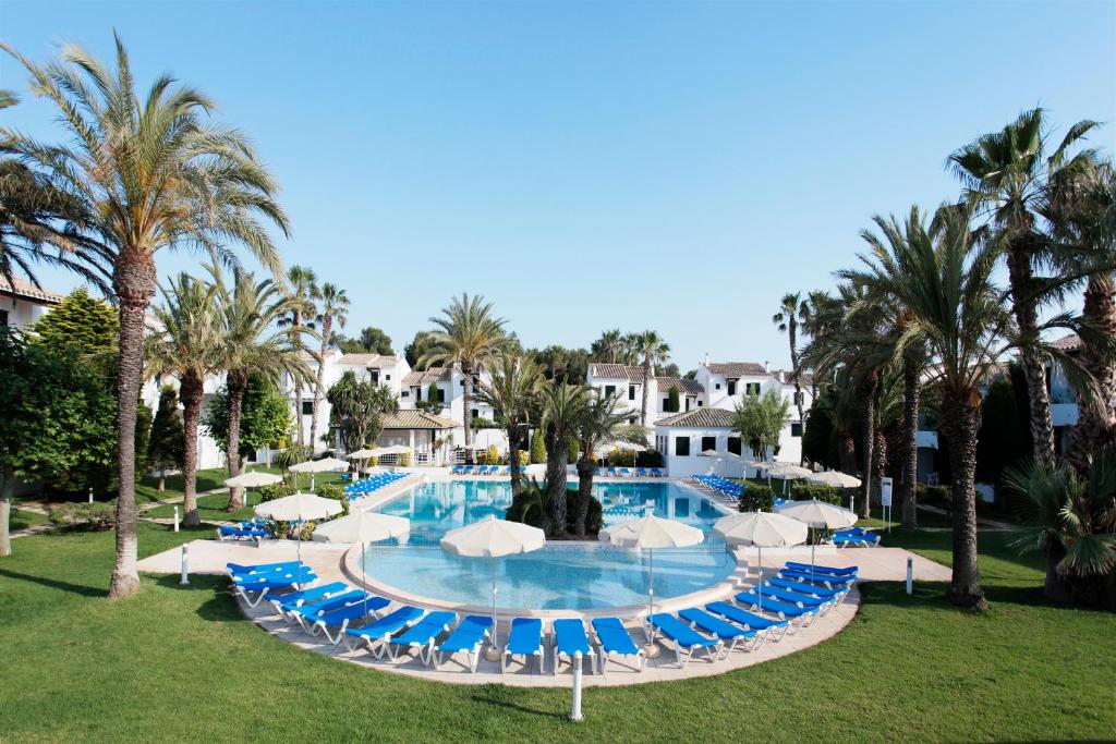松霍里吉尔梅诺卡岛俱乐部集团酒店的一个带蓝色椅子和遮阳伞的游泳池,并种植了棕榈树