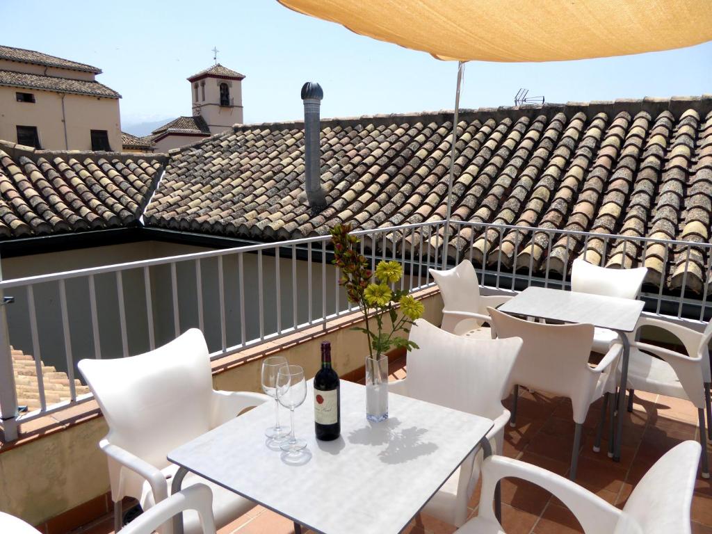 格拉纳达桂冠套房公寓的阳台配有白色的桌椅和一瓶葡萄酒