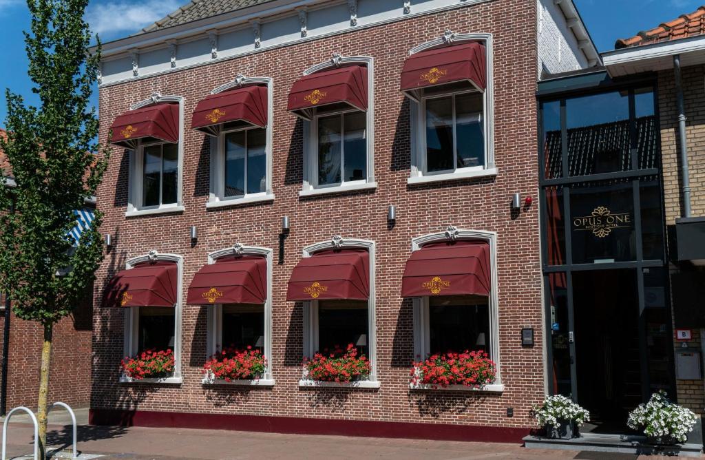 Numansdorp作品一号精品酒店的砖砌建筑,窗户上有红色遮阳篷和鲜花
