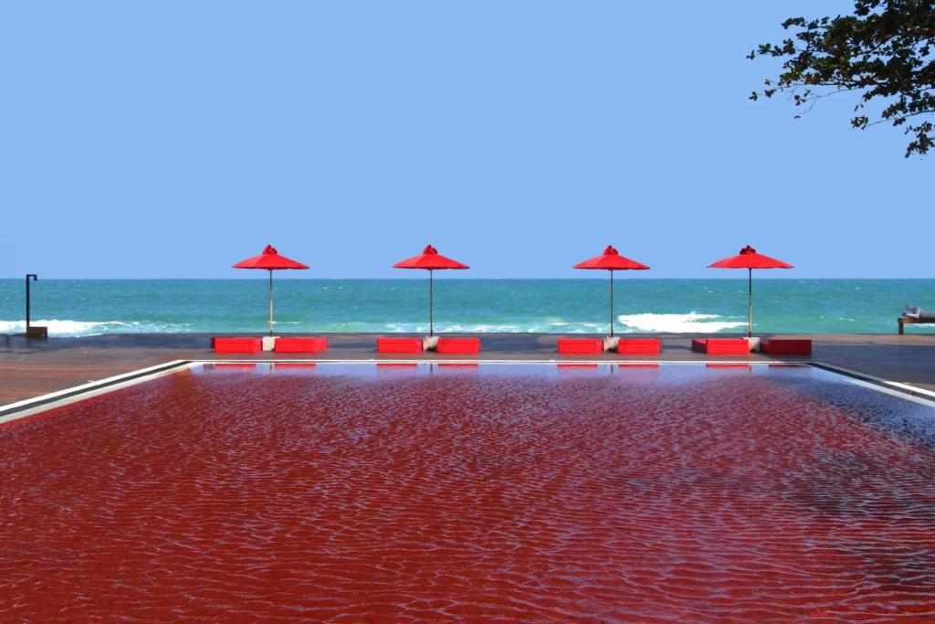 查汶The Library - SHA Extra Plus的海滩上一个带红色椅子和遮阳伞的游泳池