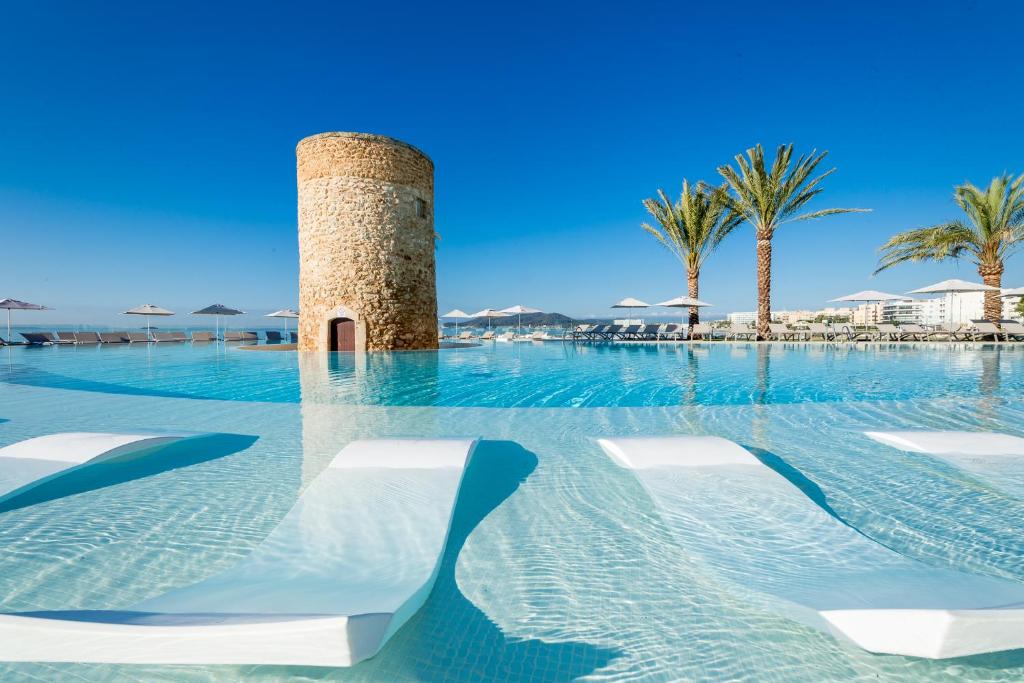 普拉亚登博萨Hotel Torre del Mar - Ibiza的一个带椅子的游泳池和水中的一个塔