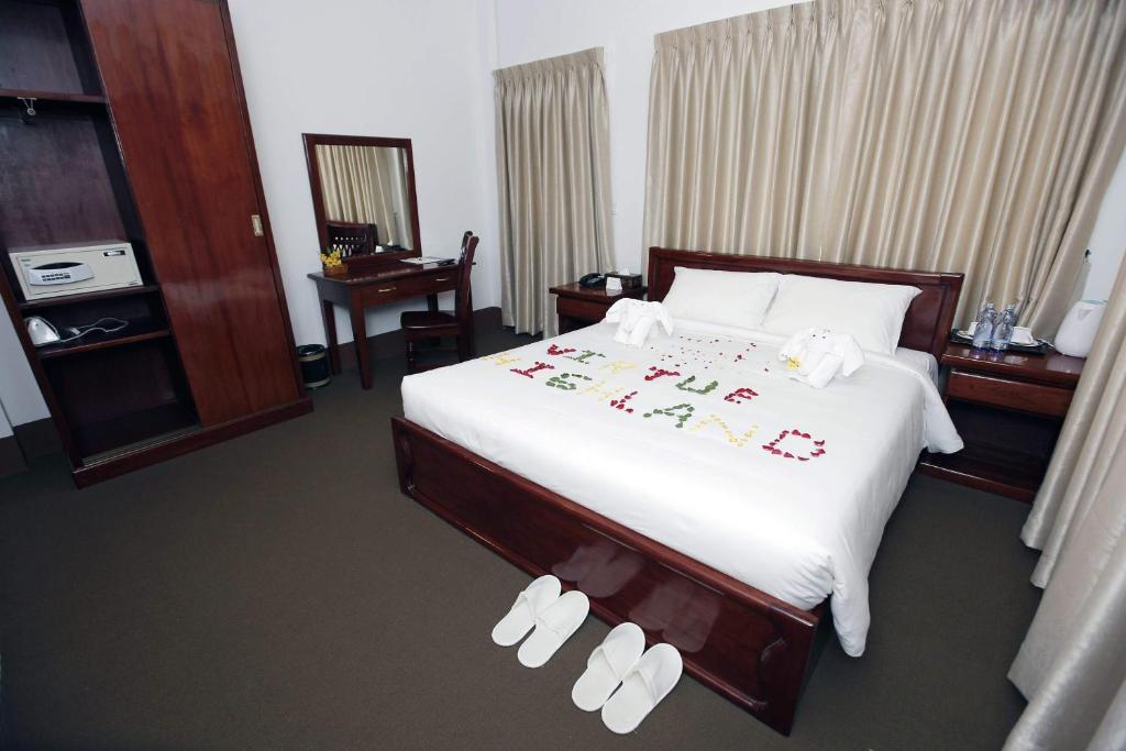 仰光高地美德酒店 的一间卧室配有一张带白色床单和拖鞋的大床。
