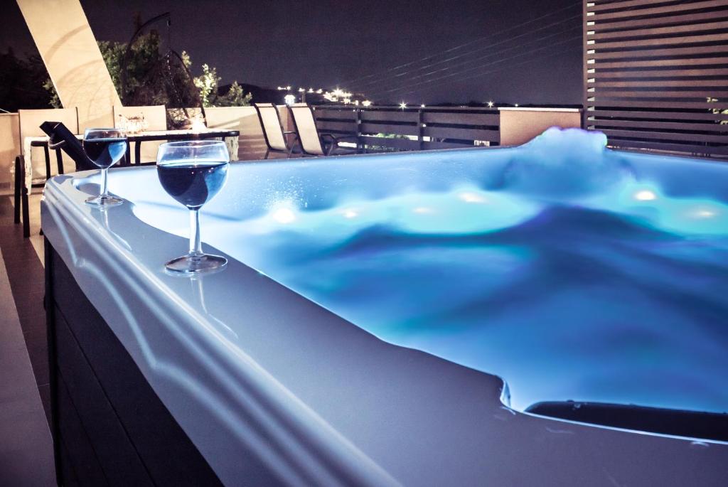 RoumelíAndromache Villas的阳台上的热水浴缸和一杯葡萄酒