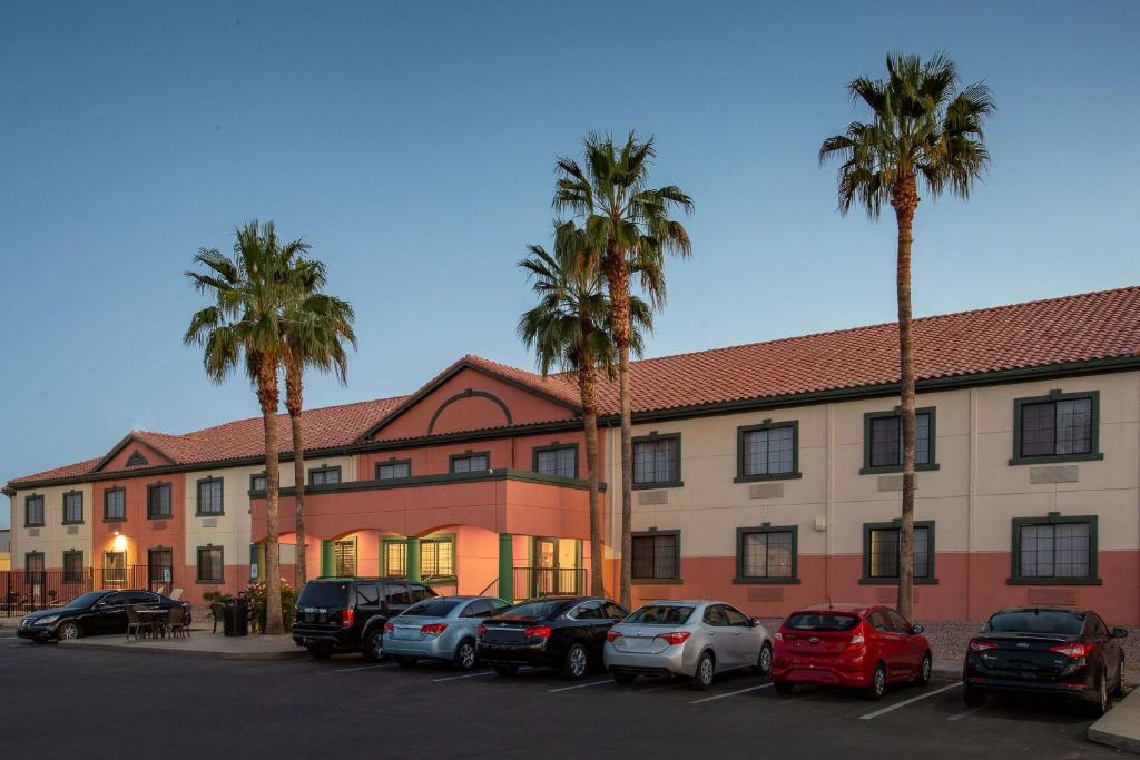 凤凰城51号大街贝蒙特旅馆套房酒店的一座有汽车停放在棕榈树停车场的建筑
