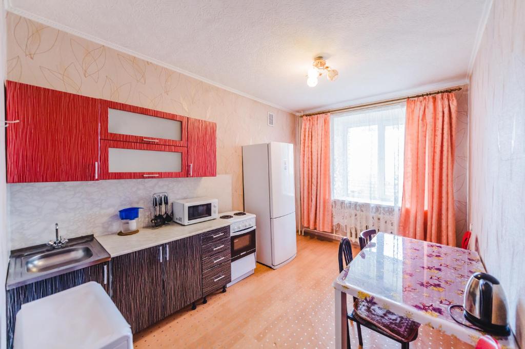 赤塔Dekabrist Apartment Shilova 46的厨房配有红色橱柜、桌子和冰箱