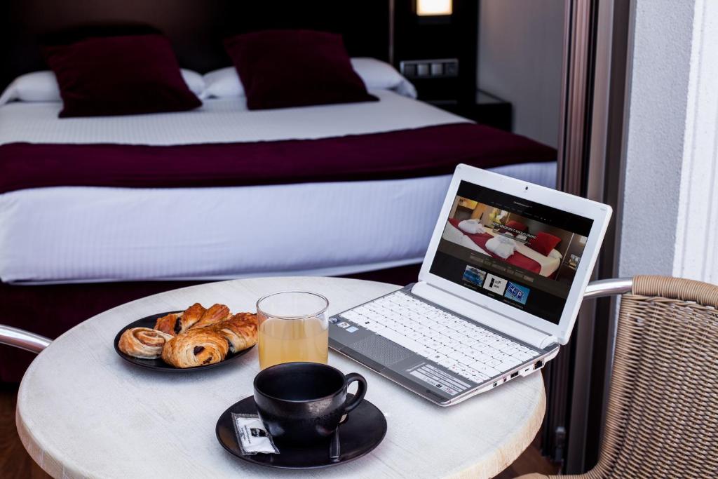 马德里克莱门特巴拉哈斯酒店的一张桌子,上面放着一台笔记本电脑,还有一杯咖啡和羊角面包