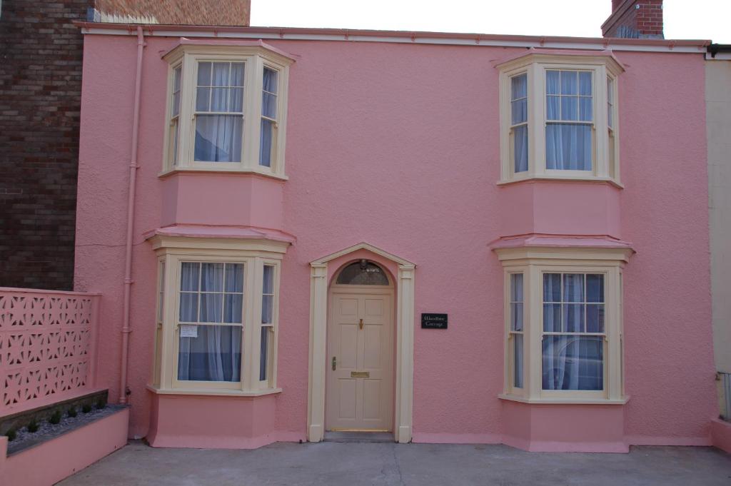 滕比Woodbine Cottage的粉红色的房子,设有白色的门和窗户