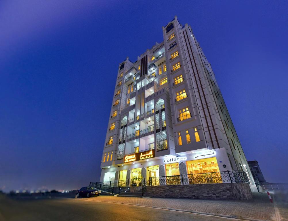 马斯喀特A'Sinamar Hotel Apartment的一座高大的建筑,晚上有很多窗户