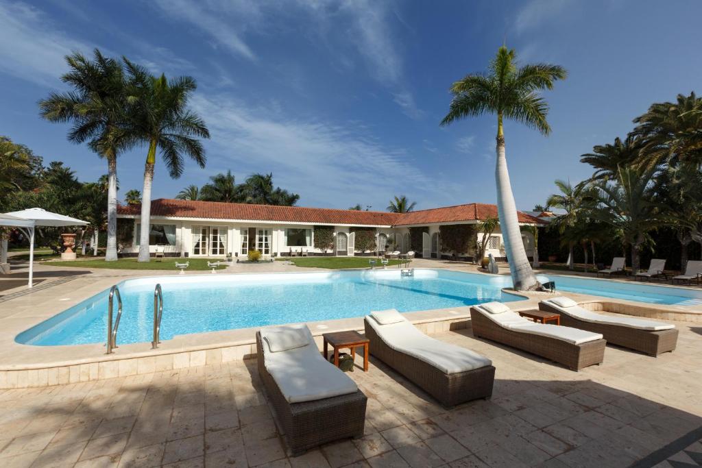 马斯帕洛马斯Magnificent Villa Piera的一座带沙发和棕榈树的游泳池,毗邻一座房子