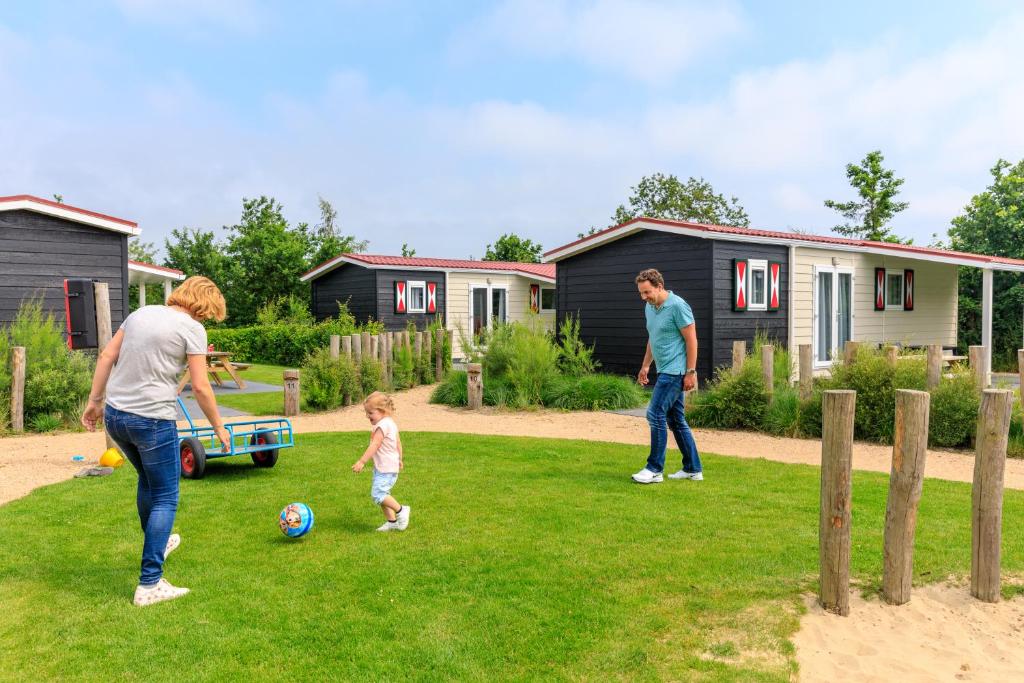 巴勒哈姆斯泰德Camping Ginsterveld的两个成年人和一个孩子在院子里玩球