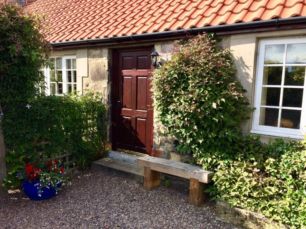 贝尔福德The Cottage的一座房子,前方设有木门和长凳