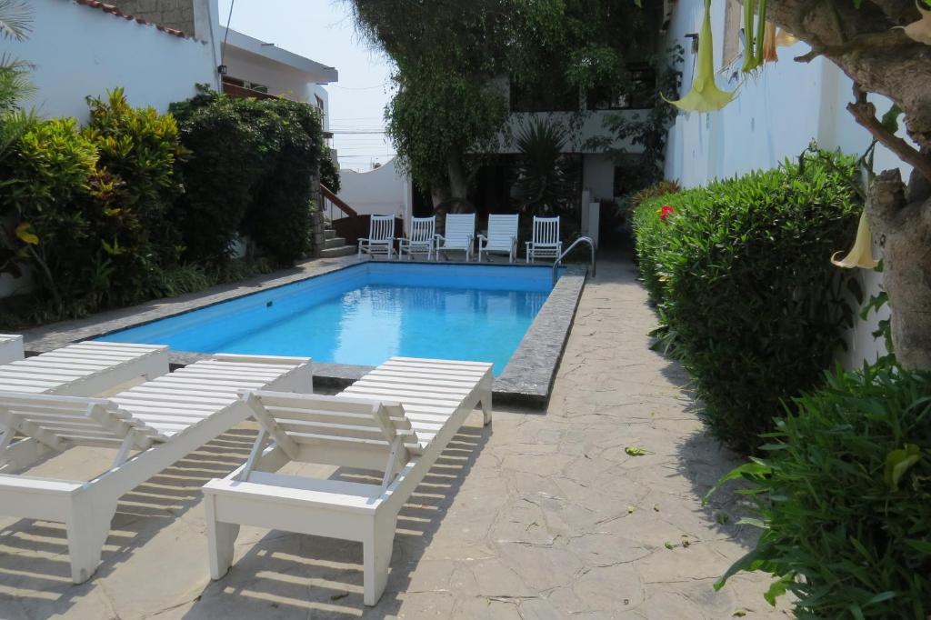 万查科Huanchaco Hostal的游泳池周围设有白色躺椅和椅子