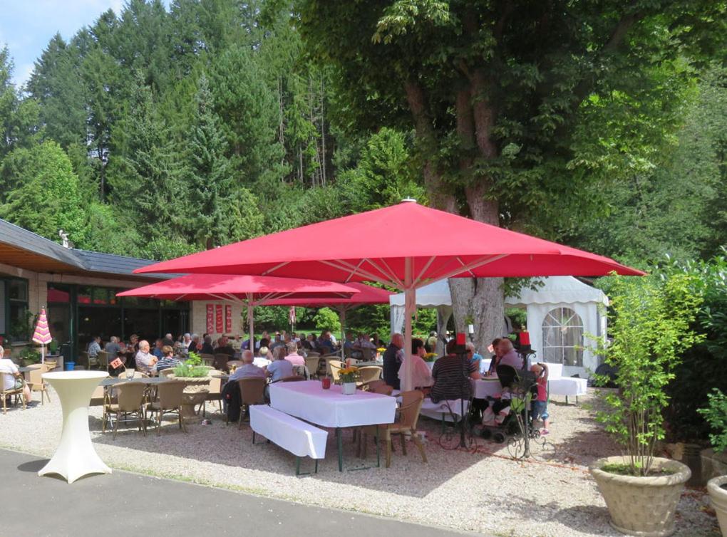 伊达尔-奥伯施泰因Diamanthotel Idar-Oberstein的一群坐在红色伞下桌子上的人