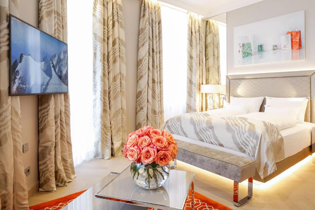 维也纳达斯蒂罗尔精品酒店的一间卧室,配有一张床,一张桌子上放着玫瑰花瓶