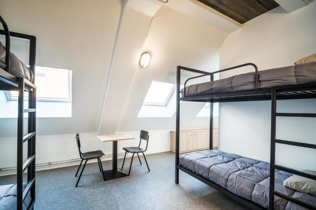 沙勒罗瓦Auberge de Jeunesse Charleroi Youth Hostel的客房设有双层床和桌椅。
