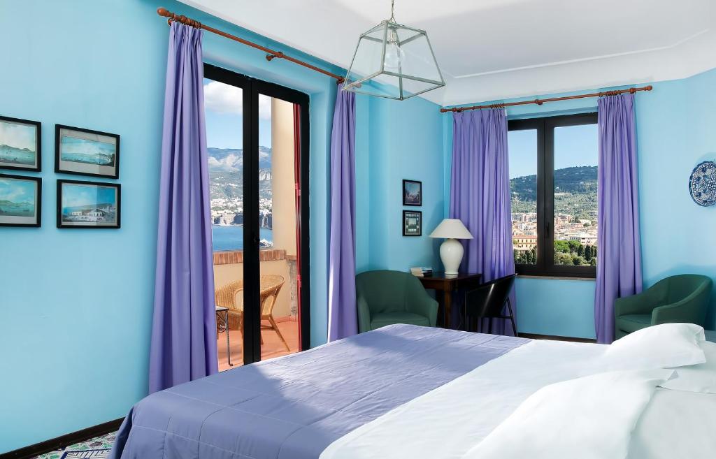 索伦托密涅瓦酒店的一间卧室设有蓝色的墙壁和一张带紫色窗帘的床