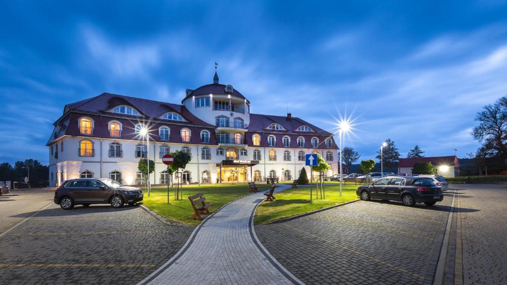 卢布涅维采沃茵斯基Spa酒店的一座大型建筑,前面有汽车停放