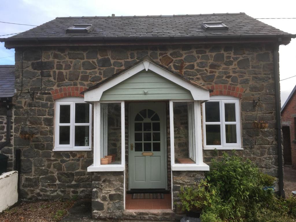 威尔斯浦Maesnewydd Cottage的石头小屋设有绿色的门和窗户