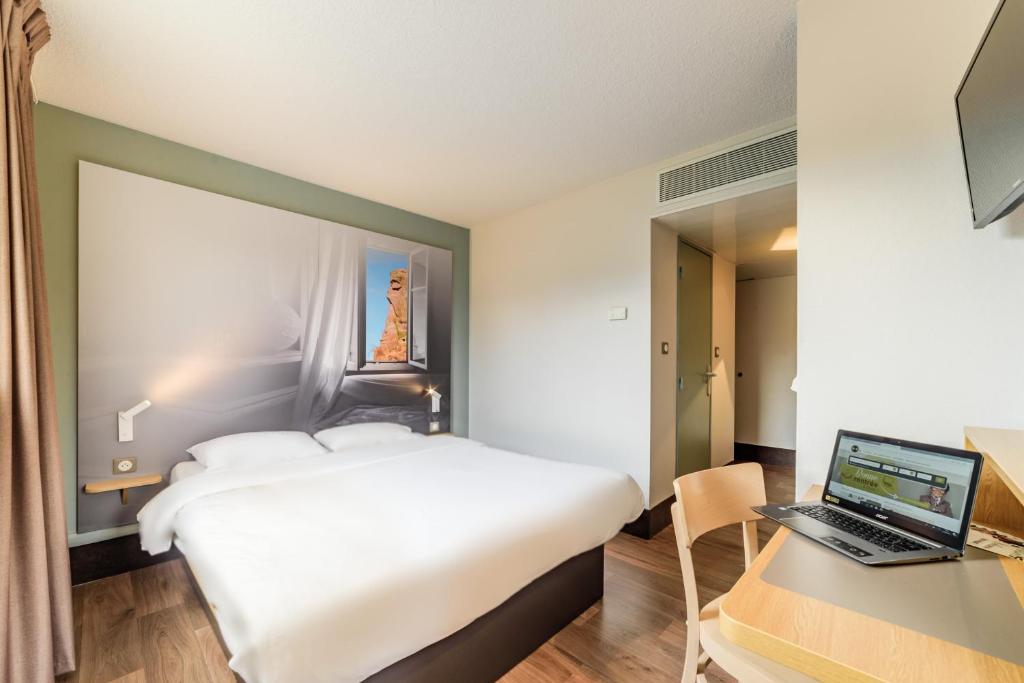 贝尔福B&B HOTEL Belfort的酒店客房配有一张床、一张书桌和一台笔记本电脑