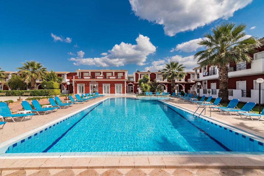 拉加纳斯Yakinthos Hotel的一座带椅子和棕榈树的游泳池以及一座建筑