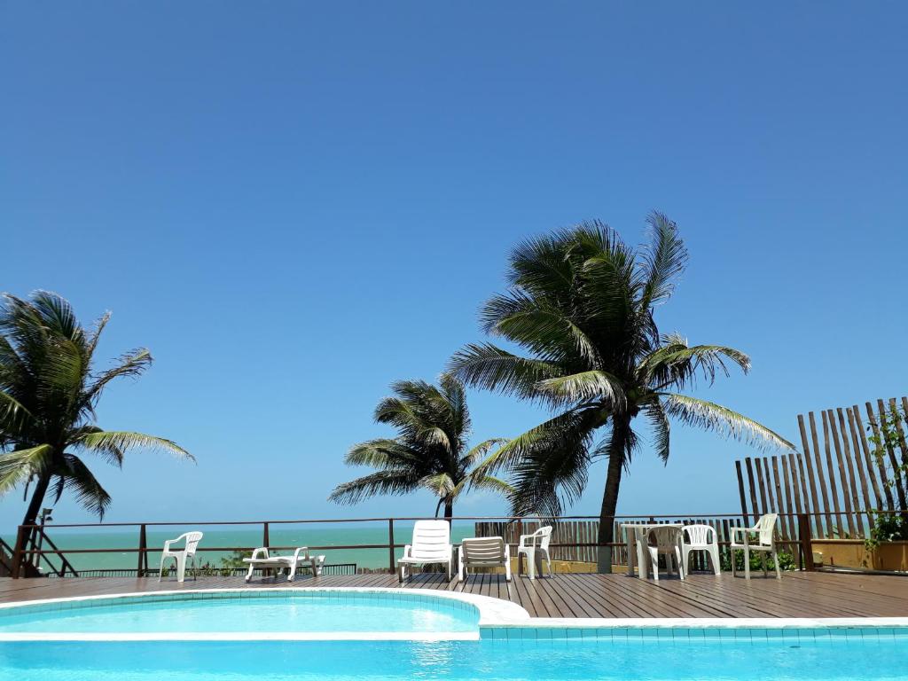纳塔尔Atlântico flat 214的毗邻大海的游泳池,游泳池配有椅子和棕榈树