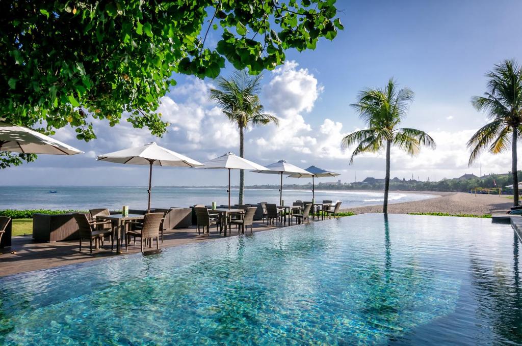 库塔巴厘岛花园海滩假日酒店的一个带桌子和遮阳伞的游泳池以及海滩
