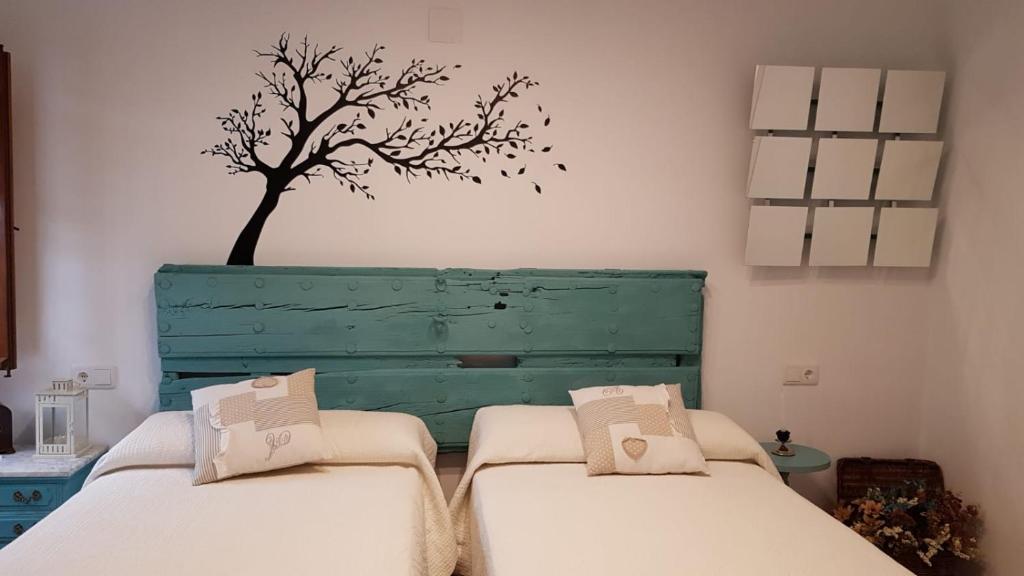 科尔多瓦El Patio De La Aljama的墙上有一棵树的房间里,有两张床