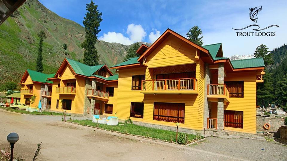 GhumlaTrout Lodges的一座黄色的大型建筑,设有绿色屋顶