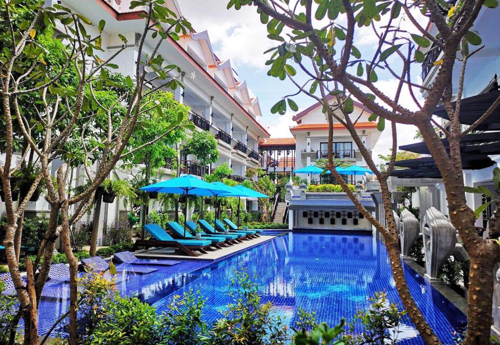 暹粒Khmer Mansion Residence的一座带椅子和遮阳伞的游泳池位于一座建筑旁边