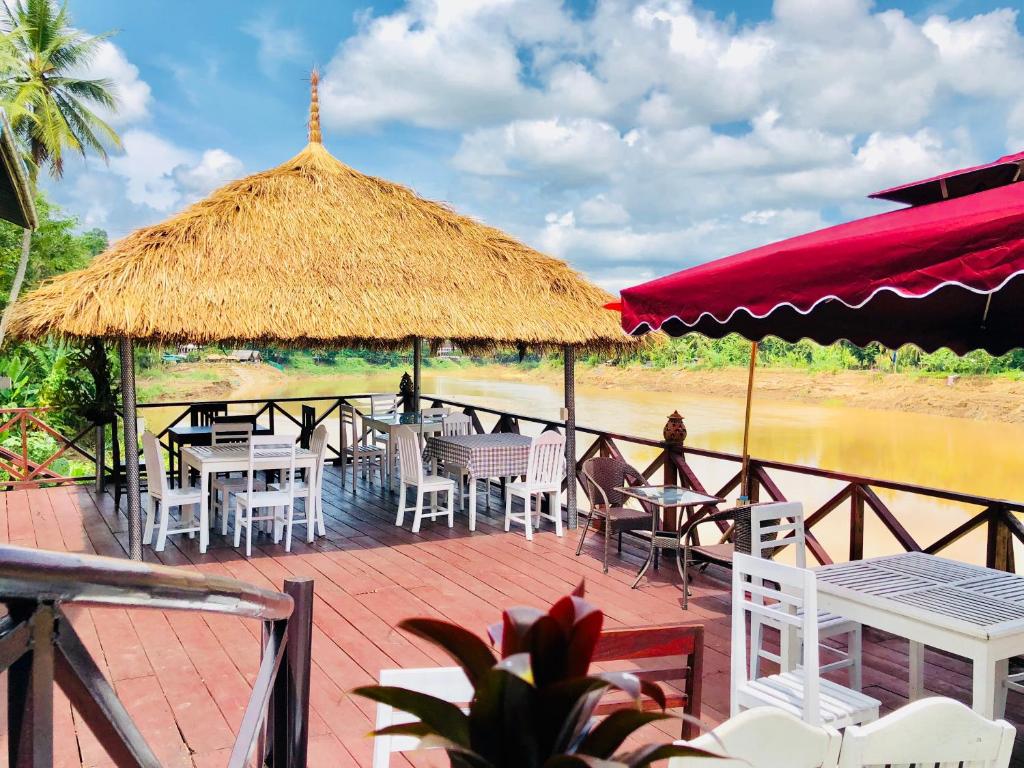 琅勃拉邦河畔快乐旅馆的一个带桌椅和稻草伞的甲板