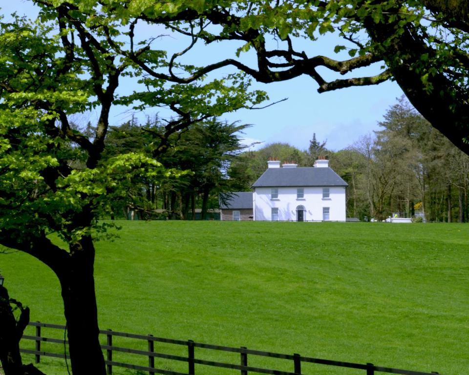 麦克鲁姆坎纳威之家住宿加早餐旅馆的绿色田野上的白色房屋,带栅栏